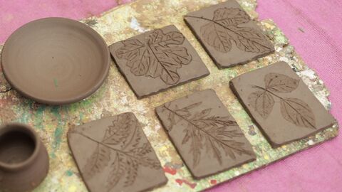 A collection of handcrafted pottery and leaf impression clay tiles on a textured surface.