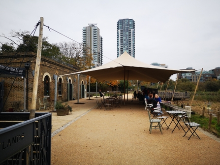 External view of the Coal House Cafe at Woodberry Wetlands. With outdoor seating and a stretch tent canopy