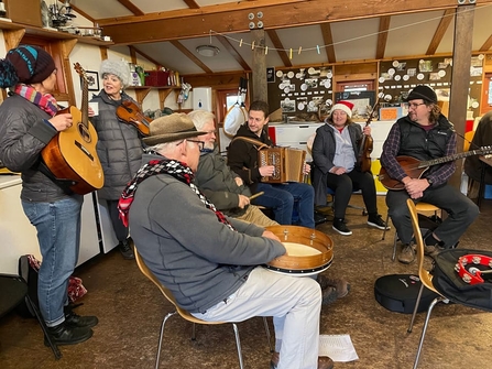 The band Larkin' the Woods playing at Centre for Wildlife Gardening on Tree Day - the band is sat on chairs playing various instruments