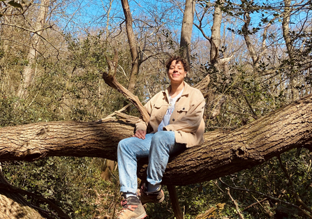 Young person sitting on a fallen tree in woodland scene