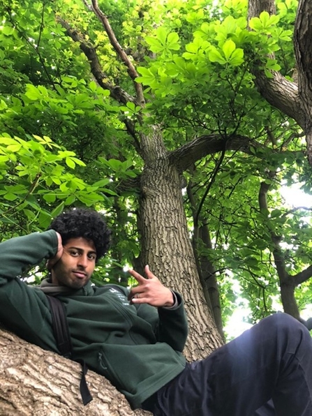 A young trainee on site leaning on a tree trunk.