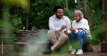 Trainees Nazia & von sitting on tree stumps surrounded by trees.