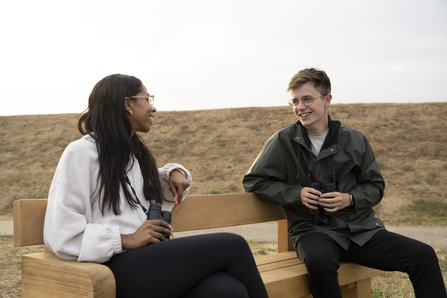 Two people sitting on a bench smiling and holding binoculars