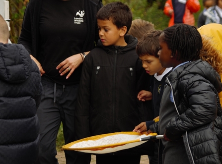 A group of children stand holding a net looking eagerly at something off camera