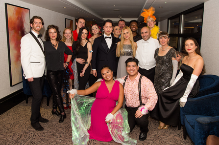 A group of people stand smiling wearing ballroom dresses and suits 