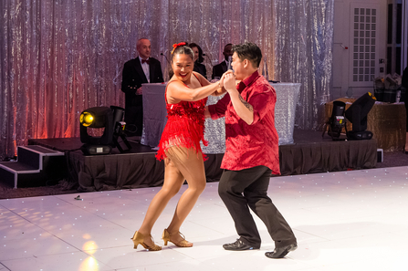 Two people ballroom dance wearing a red dress and a red shirt with black trousers