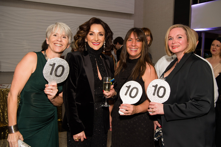 Shirley Ballas stands between three people holding sparkly judging signs with the number 10