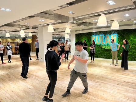 A group of couples stand in a dance hall practicing dance moves