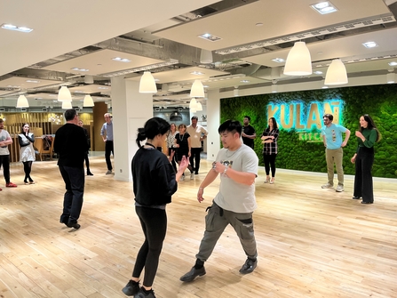 A group of couples stand in a dance hall practicing dance moves