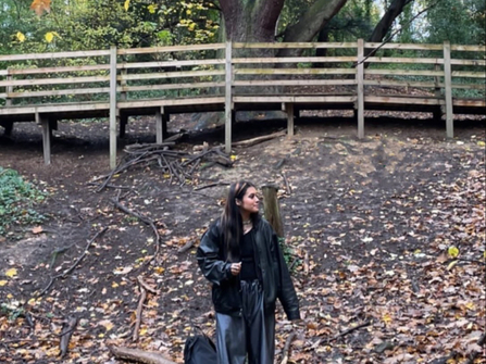 A person stood in the woods below a wooden bridge