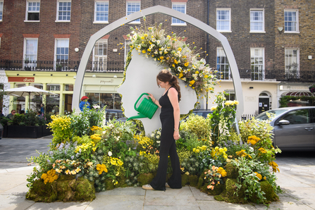 A silhouette of the queens head in a floral installation surrounded by yellow flowers