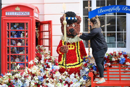 A floral installation of a bear made out of flower surrounded by flowers spilling out of a telephone box