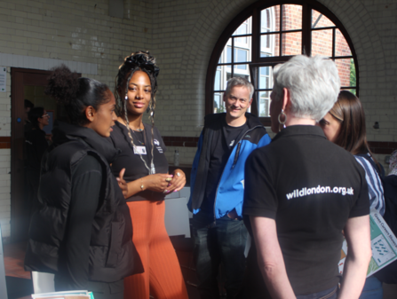 A group of people stood in a tiled room having a conversation