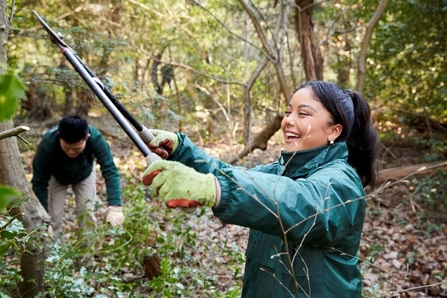 A person smiling using large secateurs to trim a tree