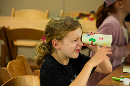 a child holding a cardboard tube holding it up to their eye and looking through it