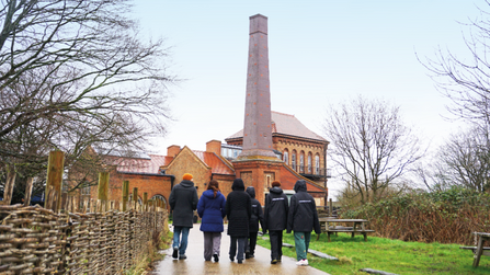 Group of young people walking in Walthamstow Wetlands towards the Engine House, with one of the Nature in Mind leaders.
