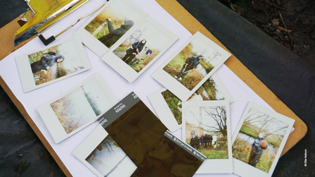 Set of polaroid photos lying on top of a clipboard. Polaroid images show snaps that have been taken of young people during a Nature in Mind session at Walthamstow Wetlands.
