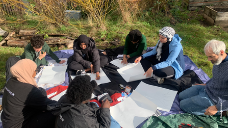 Group of young people sat in a circle on the ground, working on a drawing project for a Nature in Mind session at Walthamstow Wetlands.