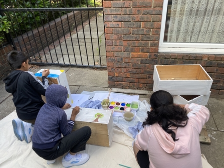 three young people at after school club in Poplar painting planters in preparation for the wildlife garden.