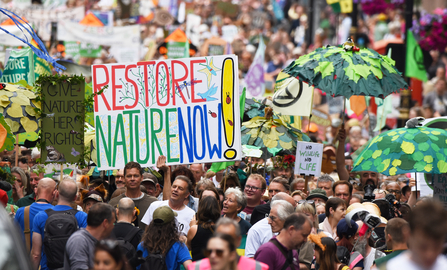 A large crowd of people with a large sign that says restore nature now