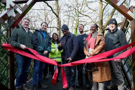 A group of people on a bridge about to cut a big red ribbon