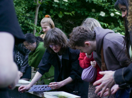 A group of young people gathered around a pond looking in to it 