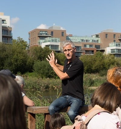 Mathew Frith sitting on a fence by Woodberry Wetlands giving a talk