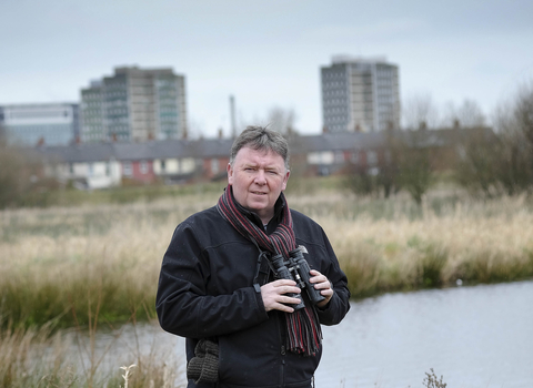 Aidan stands with his binoculars on a reserve