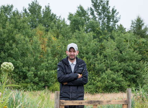 John stands besides a gate on a reserve