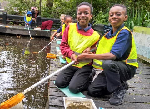 Two school children smiling whilst pond dipping at Camley Street Natural Park