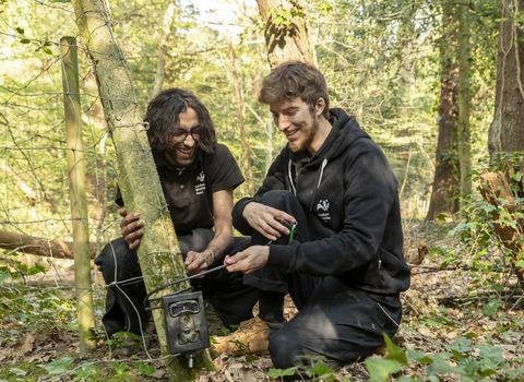 Two Keeping it Wild Trainees learning how to use a camera trap in the woods