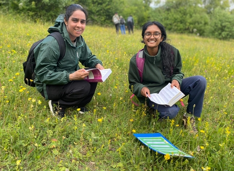 Two young people on a wild flower covered hill smiling whilst holding species identification books.