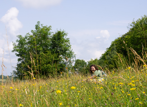 A young woman sitting smiling in a grassy meadow filled with wildflowers