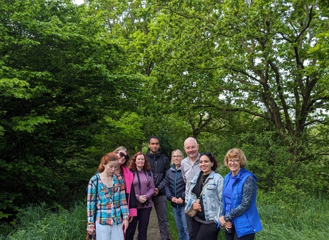 A group of 8 people standing in the clearing of a woodland in summer