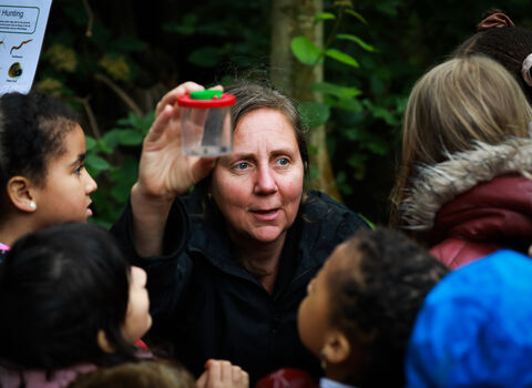 London Wildlife Trust staff member outdoors showing children a bug in a pot