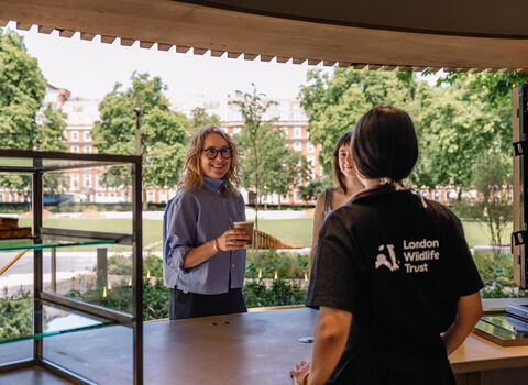 Two women standing at a kiosk with coffee, green garden in the background